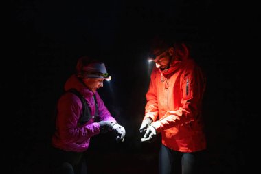 Gece yürüyüşçüleri, düşük ışık koşulları altında navigasyon ve takım çalışmasını vurgulayan far ışığı altında bir cihazı incelerler..