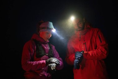 Gece yürüyüşçüleri, düşük ışık koşulları altında navigasyon ve takım çalışmasını vurgulayan far ışığı altında bir cihazı incelerler..