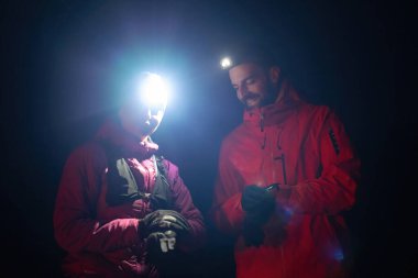 Gece yürüyüşçüleri, düşük ışık koşulları altında navigasyon ve takım çalışmasını vurgulayan far ışığı altında bir cihazı incelerler..
