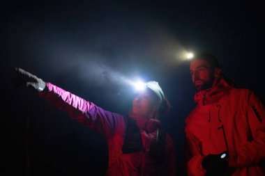 Bir kadın, kruvazör farlarının altında yürüyüş partneriyle yol tarifi tartışırken mesafeyi işaret eder.