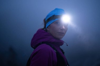 Geceleri engebeli dağ arazisinde koşan bir kadın patikası, bir far ışığıyla aydınlatılan yolu.