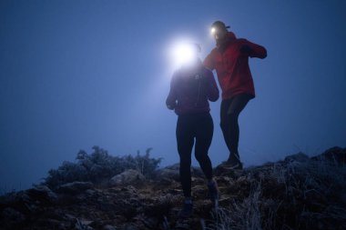 İki sporcu gece boyunca engebeli dağ patikalarında koşar, far ve kış giysileri giyerek, soğuk, sisli arazide kararlılık ve dayanıklılıkla yol alırlar..