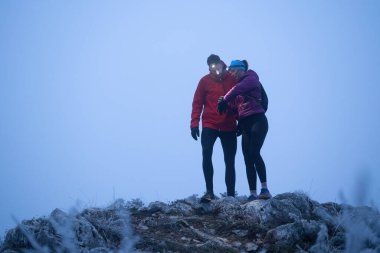 İki yürüyüşçü, sabahın erken saatlerinde bir dağın zirvesinde, etrafı sisle çevrili farlarla GPS cihazlarına danışırlar..