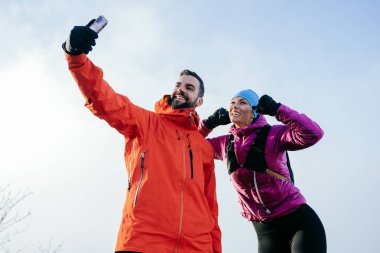 Neşeli bir çift dağ zirvesinde neşeli bir selfie çekip yürüyüşlerini eğlenceli hareketlerle kutluyor.