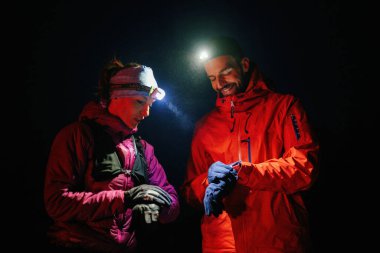 Gece yürüyüşçüleri, düşük ışık koşulları altında navigasyon ve takım çalışmasını vurgulayan far ışığı altında bir cihazı incelerler..
