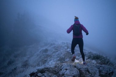 Geceleri engebeli dağ arazisinde koşan bir kadın patikası, bir far ışığıyla aydınlatılan yolu.