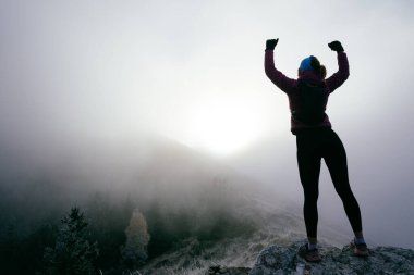 Kayalık dağların zirvesinde zafer kollarıyla sisle çevrili bir kadın kutluyor..