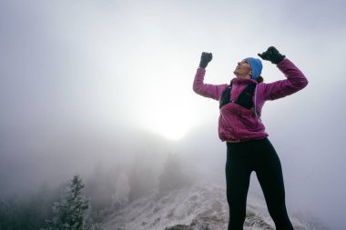 Kayalık dağların zirvesinde zafer kollarıyla sisle çevrili bir kadın kutluyor..