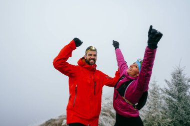 İki yürüyüşçü, uzun bir gece yolculuğunun ardından sevinç ve başarı göstererek, dağların zirvesinde kollarını kaldırır..