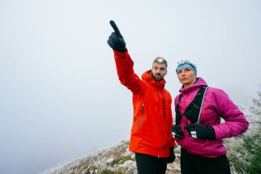 Erkek, kadınla yürürken işaret ediyor. Erkek, sisli bir dağ yamacında kadın bir partnerle yürürken işaret ediyor..