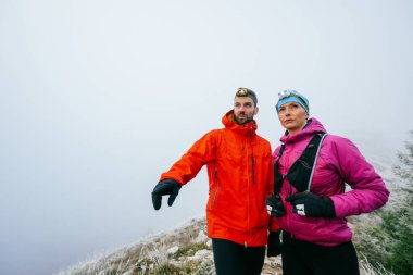 Erkek, kadınla yürürken işaret ediyor. Erkek, sisli bir dağ yamacında kadın bir partnerle yürürken işaret ediyor..