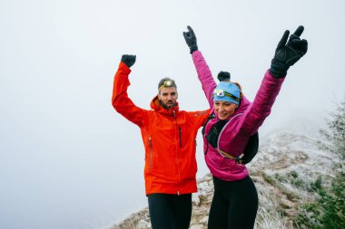 İki yürüyüşçü, uzun bir gece yolculuğunun ardından sevinç ve başarı göstererek, dağların zirvesinde kollarını kaldırır..