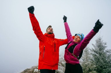 İki yürüyüşçü, uzun bir gece yolculuğunun ardından sevinç ve başarı göstererek, dağların zirvesinde kollarını kaldırır..