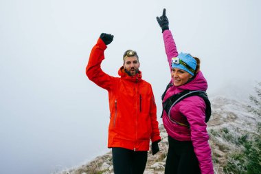 İki yürüyüşçü, uzun bir gece yolculuğunun ardından sevinç ve başarı göstererek, dağların zirvesinde kollarını kaldırır..