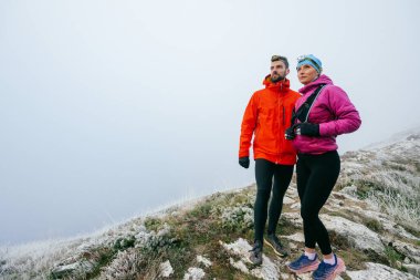 Açık hava kıyafetleri içinde sisli bir dağın tepesinde poz veren iki yürüyüşçünün portresi.