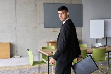 Siyah takım elbiseli kararlı bir işadamı ofisin içinde güven içinde yürüyor, profesyonelliği somutlaştırıyor ve yeni zorluklara doğru ilerlerken odaklanıyor.. 