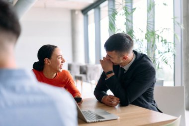 Genç, çeşitli bir iş ekibi modern bir ofiste birlikte oturuyor, fikir ve iş planlarını paylaşıyor, gelecekteki başarı için işbirliği ve yenilikleri teşvik ediyor.