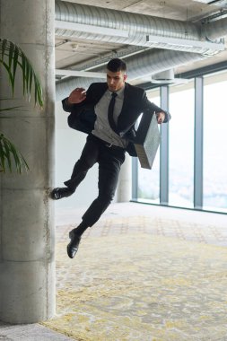Modern bir ofise kendinden geçmiş bir şekilde atlayan bir işadamı, elinde bir evrak çantasıyla, başarı ve zafer anını kutluyor.