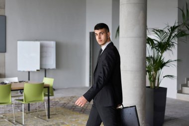 Siyah takım elbiseli kararlı bir işadamı ofisin içinde güven içinde yürüyor, profesyonelliği somutlaştırıyor ve yeni zorluklara doğru ilerlerken odaklanıyor.. 