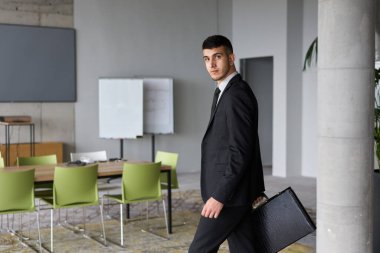 Siyah takım elbiseli kararlı bir işadamı ofisin içinde güven içinde yürüyor, profesyonelliği somutlaştırıyor ve yeni zorluklara doğru ilerlerken odaklanıyor.. 