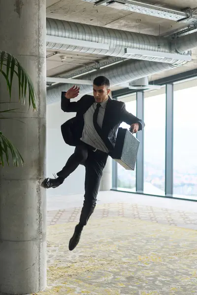 Modern bir ofise kendinden geçmiş bir şekilde atlayan bir işadamı, elinde bir evrak çantasıyla, başarı ve zafer anını kutluyor.