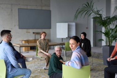 Çeşitli iş adamları modern bir ofiste dikkatle oturup, bir eğitmenin önderliğindeki bir eğitim oturumunda aktif olarak en son teknolojik gelişmelere odaklanırlar.