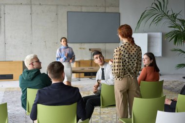 Çeşitli iş adamları modern bir ofiste dikkatle oturup, bir eğitmenin önderliğindeki bir eğitim oturumunda aktif olarak en son teknolojik gelişmelere odaklanırlar.