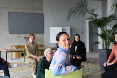 Çeşitli iş adamları modern bir ofiste dikkatle oturup, bir eğitmenin önderliğindeki bir eğitim oturumunda aktif olarak en son teknolojik gelişmelere odaklanırlar.