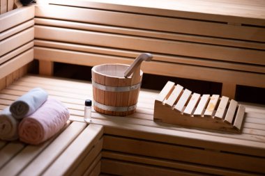 Sauna kovasına yakın, saunanın içindeki ahşap bankta rulo havluların yanında kepçe ve gerekli yağlarla..