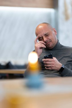 Masada oturan orta yaşlı bir adam telefonuna bakarken sıkıntılı görünüyor..