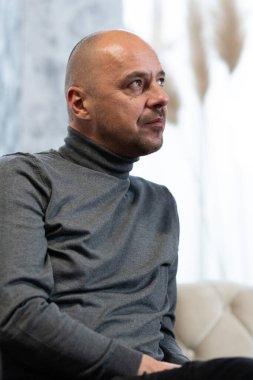 Eli çenesinde düşünen kel bir adam yukarı bakıyor, içeride oturuyor..