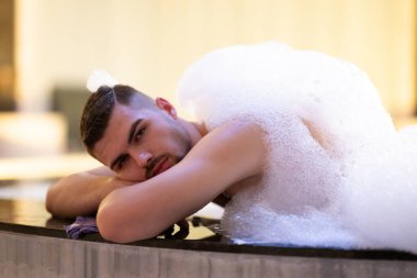 Köpük içinde dinlenen adam. Arınma ayini sırasında beyaz köpükle kaplı Türk hamamında yatan rahat adam.