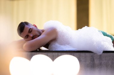 Köpük içinde dinlenen adam. Arınma ayini sırasında beyaz köpükle kaplı Türk hamamında yatan rahat adam.