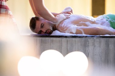 Köpüklü sırt masajı. Terapist geleneksel banyo ritüeli sırasında hastalara sabun köpüğü sürüyor.