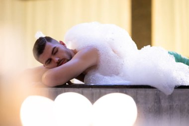 Köpük içinde dinlenen adam. Arınma ayini sırasında beyaz köpükle kaplı Türk hamamında yatan rahat adam.