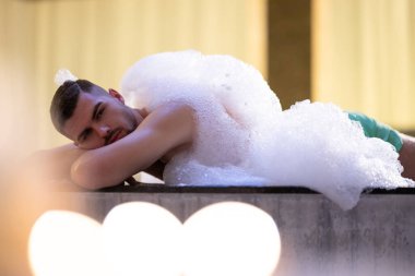 Köpük içinde dinlenen adam. Arınma ayini sırasında beyaz köpükle kaplı Türk hamamında yatan rahat adam.
