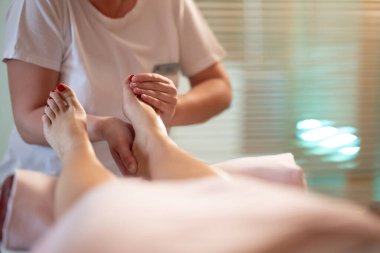 Beyaz üniformalı profesyonel bir masaj terapisti, sakin ve sakin bir spa ortamında müşteriye rahatlatıcı bir ayak masajı sağlar..