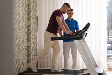 Adam içeride koşu bandında antrenör yardımıyla fizik tedavi görüyor..