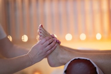 Beyaz üniformalı profesyonel bir masaj terapisti, sakin ve sakin bir spa ortamında müşteriye rahatlatıcı bir ayak masajı sağlar..