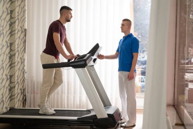 Adam içeride koşu bandında antrenör yardımıyla fizik tedavi görüyor..