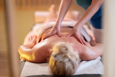 Spa 'da Sırt Masajı. Mavi üniformalı profesyonel bir masaj terapisti masaj masasında yatan bir müşteriye rahatlatıcı bir sırt masajı sağlar.