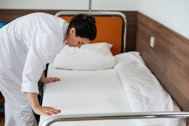 Üniformalı iki hemşire çarşafları değiştirerek ve hastalar için hijyenik bir ortam sağlayarak hastane odasını temizleyip düzenliyor.