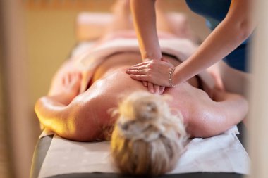 Spa 'da Sırt Masajı. Mavi üniformalı profesyonel bir masaj terapisti masaj masasında yatan bir müşteriye rahatlatıcı bir sırt masajı sağlar.