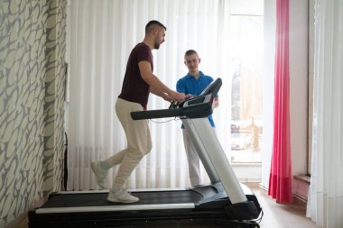 Adam içeride koşu bandında antrenör yardımıyla fizik tedavi görüyor..