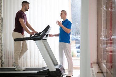 Adam içeride koşu bandında antrenör yardımıyla fizik tedavi görüyor..