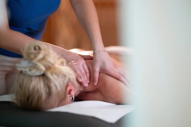 Spa 'da Sırt Masajı. Mavi üniformalı profesyonel bir masaj terapisti masaj masasında yatan bir müşteriye rahatlatıcı bir sırt masajı sağlar.