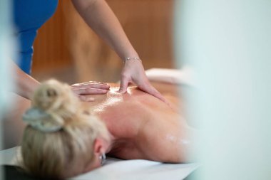 Spa 'da Sırt Masajı. Mavi üniformalı profesyonel bir masaj terapisti masaj masasında yatan bir müşteriye rahatlatıcı bir sırt masajı sağlar.