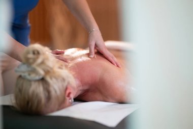 Spa 'da Sırt Masajı. Mavi üniformalı profesyonel bir masaj terapisti masaj masasında yatan bir müşteriye rahatlatıcı bir sırt masajı sağlar.