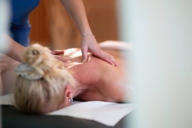 Spa 'da Sırt Masajı. Mavi üniformalı profesyonel bir masaj terapisti masaj masasında yatan bir müşteriye rahatlatıcı bir sırt masajı sağlar.