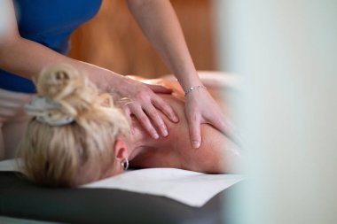 Spa 'da Sırt Masajı. Mavi üniformalı profesyonel bir masaj terapisti masaj masasında yatan bir müşteriye rahatlatıcı bir sırt masajı sağlar.